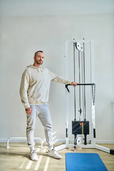 Full length of handsome man near exercise machine in gym of modern kinesiology center — Stock Photo