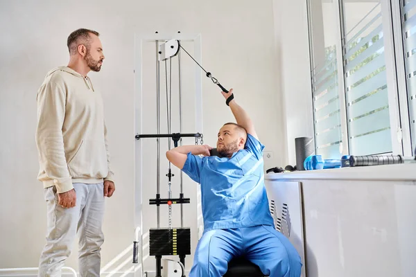 Experienced specialist training on exercise machine during consultation of man in kinesio center — Stock Photo