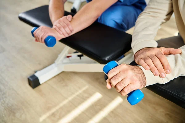 Cropped view of male patient working out with dumbbell near recovery specialist in kinesio center — Stock Photo