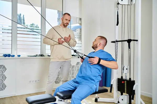 Квалифицированный специалист по реабилитации показывает упражнения на тренажере человеку в кинезиологическом центре — стоковое фото