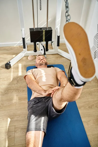 Vista de ángulo alto del hombre en la pierna de entrenamiento de ropa deportiva en la máquina de ejercicio en el centro de kinesiología - foto de stock
