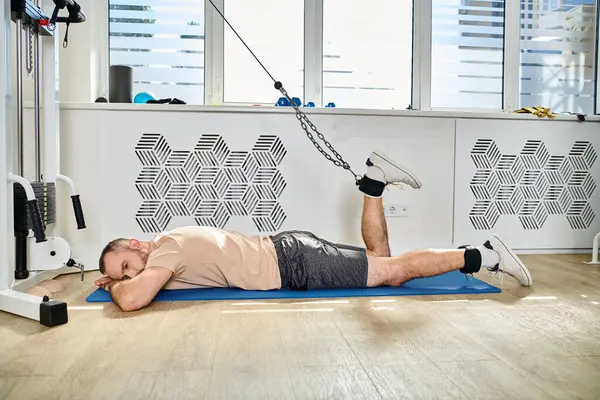 Sportive man in lying down on fitness mat and training leg on exercise machine in kinesio center — Stock Photo