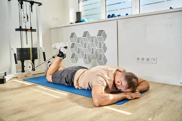 Male patient of kinesio center lying face down on fitness mat and training on exercise machine — Stock Photo