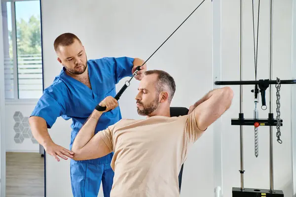Опытный физиотерапевт помогает человеку с восстановлением тренировки на тренажере в центре Кинезио — стоковое фото