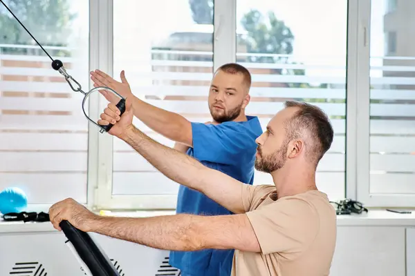 Professional instructor in blue uniform assisting man during recovery training in kinesio center — Stock Photo