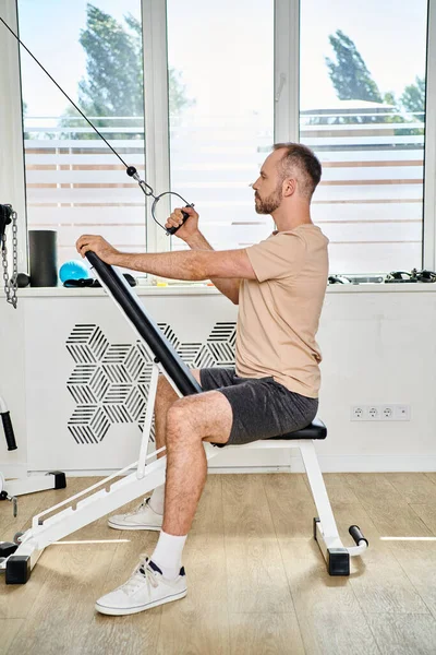 Seitenansicht eines gutaussehenden bärtigen Mannes in Sportbekleidung beim Training an einem Trainingsgerät im Kinesio Center — Stockfoto