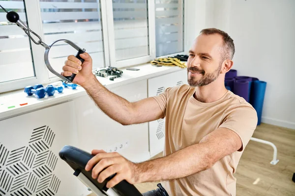 Lächelnder Mann im Sportkleidungstraining auf modernem Trainingsgerät, glücklicher Patient des Kinesio-Zentrums — Stockfoto