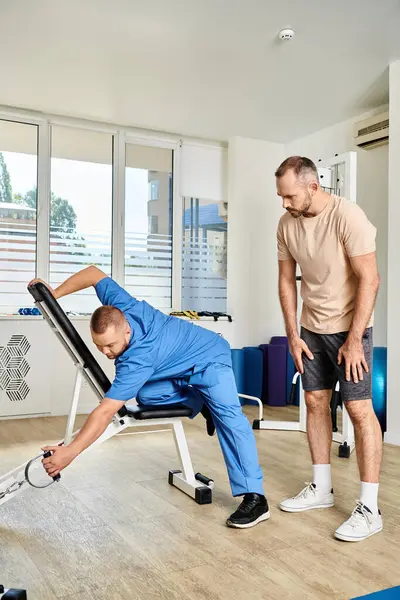 Recovery specialist in blue uniform showing how to train on exercise machine in kinesiology center — Stock Photo