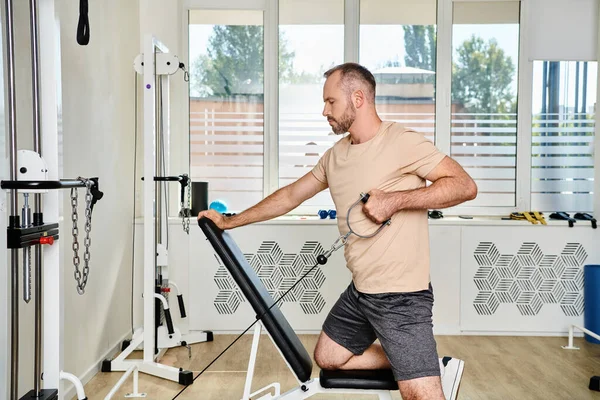 Side view of bearded man in sportswear working out on exercise machine, recovery in kinesio center — Stock Photo