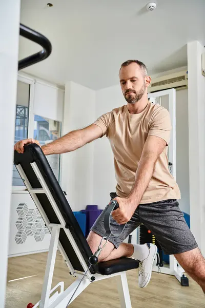 Handsome man in sportswear training on exercise machine in modern gym of kinesio center, recovery — Stock Photo