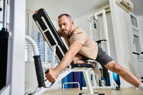 Bearded man in sportswear training on exercise machine in modern gym of kinesio center, recovery — Stock Photo