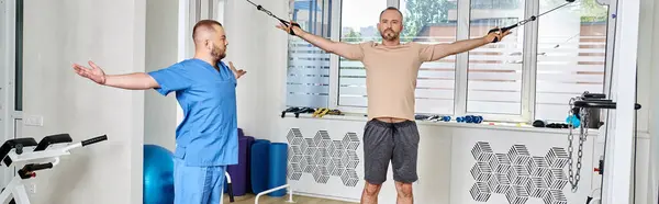 Assistente di recupero che aiuta l'uomo nella formazione di abbigliamento sportivo sulla macchina esercizio nel centro di kinesio, banner — Foto stock