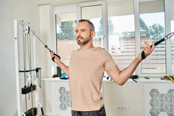 Sportlich gut aussehender Mann trainiert Arme auf modernem Trainingsgerät im Kinesio-Zentrum, Erholung Fitness — Stockfoto