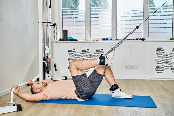 Side view of man in sportswear lying down on fitness mat during recovery training in kinesio center — Stock Photo