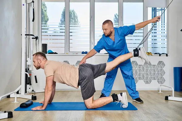 Physiothérapeute qualifié assistant l'entraînement de l'homme pendant la séance de récupération dans la salle de gym du centre de kinésithérapie — Photo de stock