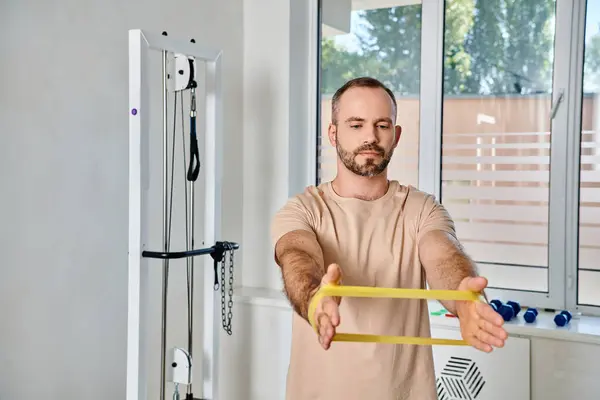 Athletic bearded man training with resistance band in kinesiology center, recovery session — Stock Photo