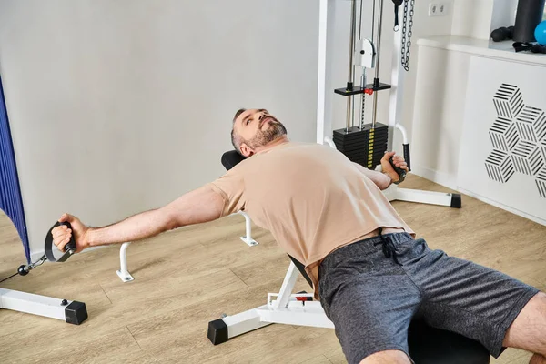 Bearded man in sportswear working out on exercise machine in kinesio center, recovery session — Stock Photo