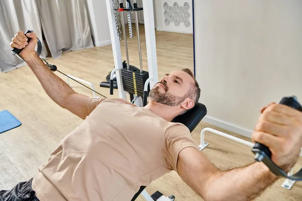 Bearded man in sportswear training arms on exercise machine in kinesio center, recovery session — Stock Photo