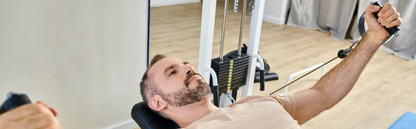 Handsome man in sportswear training arms on exercise machine in kinesio center, banner — Stock Photo