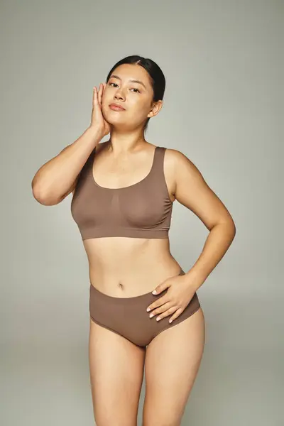 Charmante jeune femme asiatique aux cheveux bruns posant en lingerie marron sur fond gris neutre — Photo de stock