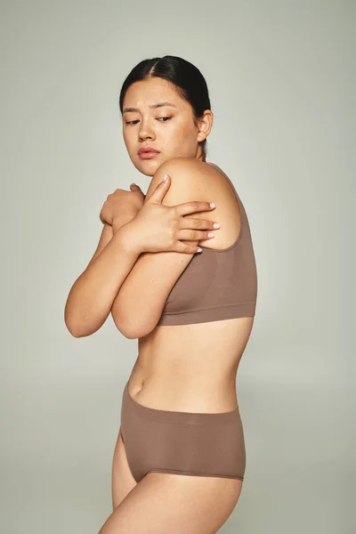 Shy asian woman in underwear covering body while embracing herself on grey background, body shaming — Stock Photo