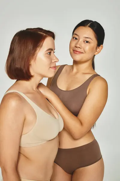 Heureux asiatique femme en sous-vêtements embrassant son ami sur fond gris, beauté et corps positif — Photo de stock