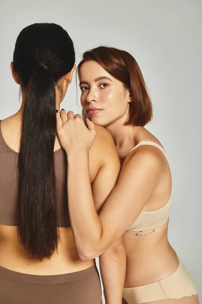 Junge Frau mit kurzen Haaren umarmt brünette Freundin auf grauem Hintergrund, Körper positiv — Stockfoto