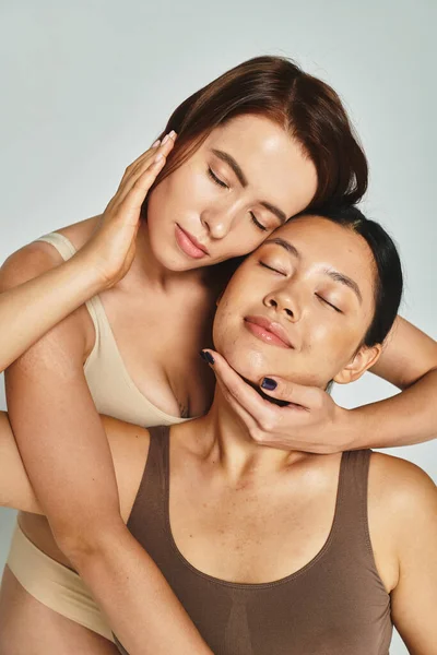 Young and multicultural friends in underwear embracing each other on grey background, beauty — Stock Photo