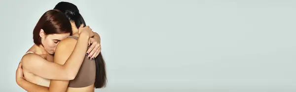 Young woman with closed eyes embracing her friend while showing support on grey background, banner — Stock Photo