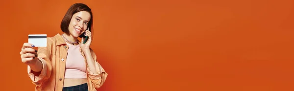 Femme heureuse parlant sur smartphone et tenant la carte de crédit sur fond orange, bannière shopping — Photo de stock