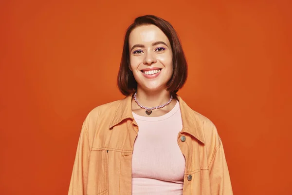 Fröhliche junge Frau mit kurzen Haaren, die in die Kamera blickt und auf orangefarbenem Hintergrund lächelt, unbeschwert — Stockfoto