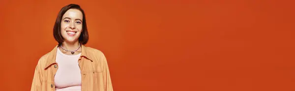 Fröhliche junge Frau mit kurzen Haaren, die in die Kamera blickt und auf orangefarbenem Hintergrund lächelt, Banner — Stockfoto