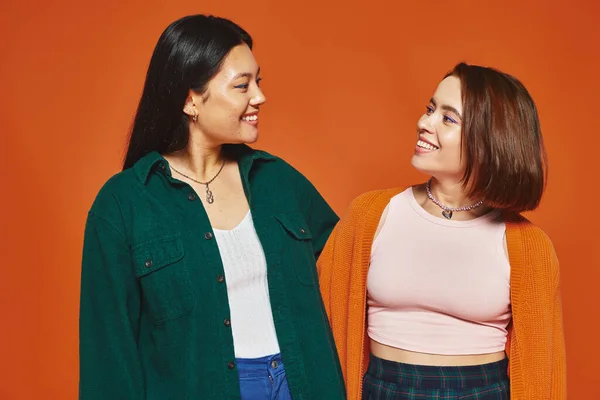 Fröhliche Frauen in lässiger Kleidung, die sich umarmen und glückliche Momente miteinander auf orangefarbenem Hintergrund teilen — Stockfoto