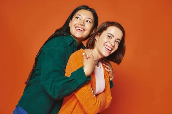 Due amiche in abbigliamento casual abbracciare e condividere momento felice insieme su sfondo arancione — Foto stock