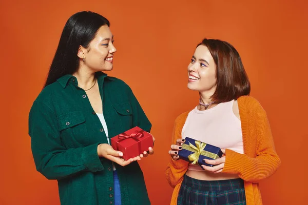 Femmes multiethniques échangeant des cadeaux, souriant et appréciant mutuellement compagnie sur fond orange — Photo de stock