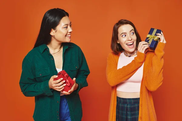 Multicultural amigos do sexo feminino trocando presentes, sorrindo e se divertindo no fundo laranja — Fotografia de Stock