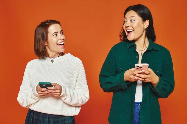 Multicultural young women using smartphones on vibrant orange background, using social media — Stock Photo