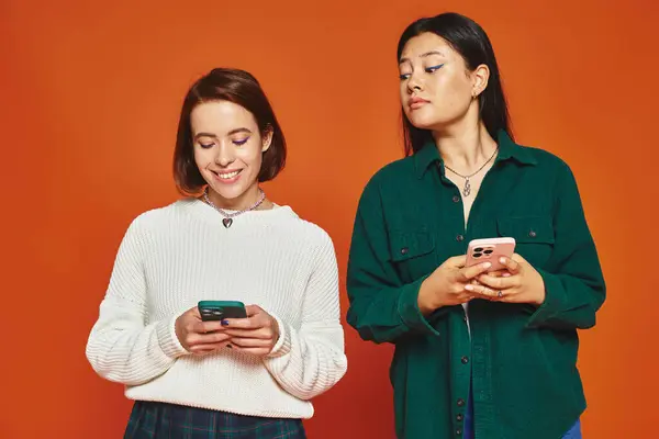 Мультикультурні молоді жінки використовують смартфони на яскравому помаранчевому фоні, користувачі соціальних мереж — стокове фото