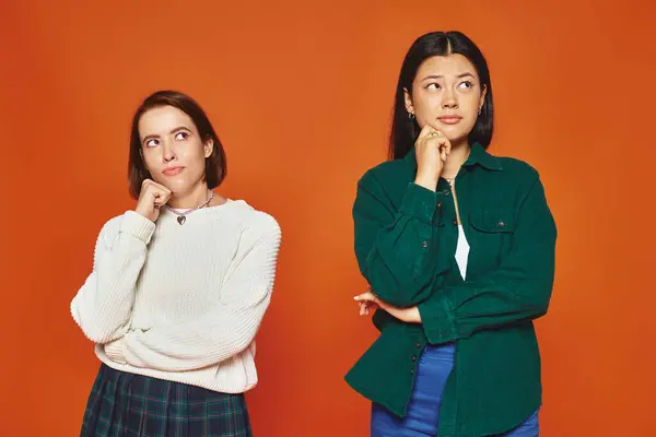 Pensive young multicultural friends in vibrant attire looking away on orange background, think — Stock Photo
