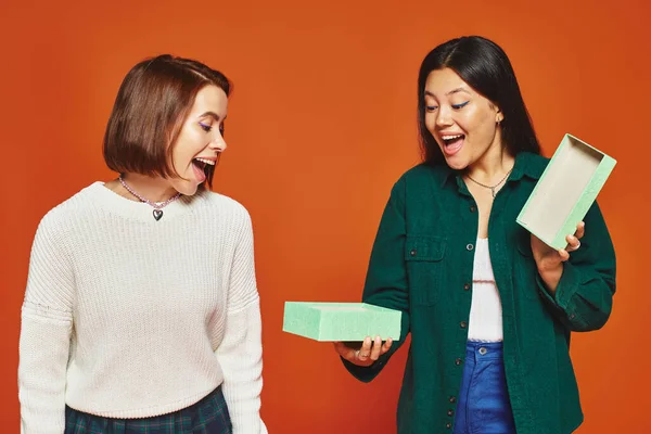 Eccitata donna asiatica apertura regalo vicino felice amica femminile su sfondo arancione, regalo dare — Foto stock