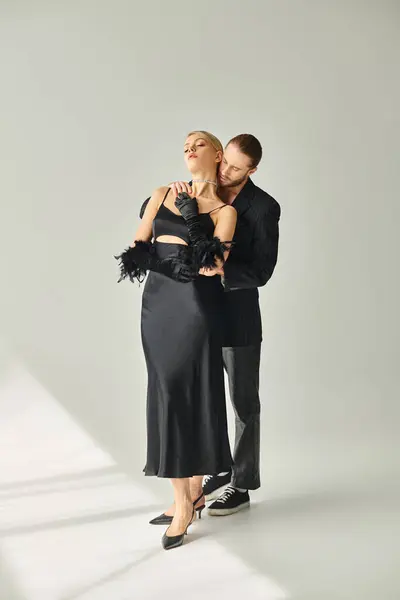Привлекательная сексуальная пара в элегантных черных одеждах позируют вместе и обнимаются с любовью на сером фоне — стоковое фото