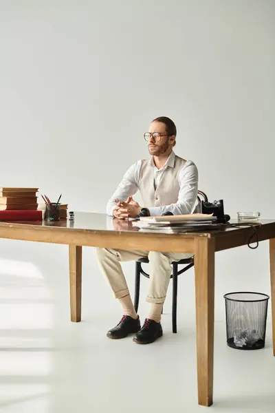 Atractivo joven con barba y gafas con el pelo recogido sentado en la mesa en su oficina - foto de stock
