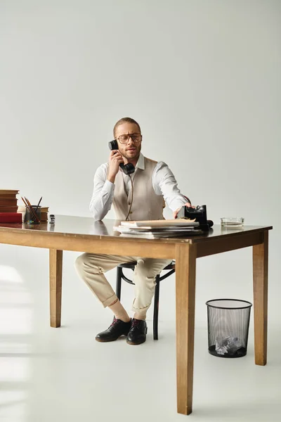 Atractivo hombre guapo con barba y gafas sentado en la mesa y hablando por teléfono vintage - foto de stock