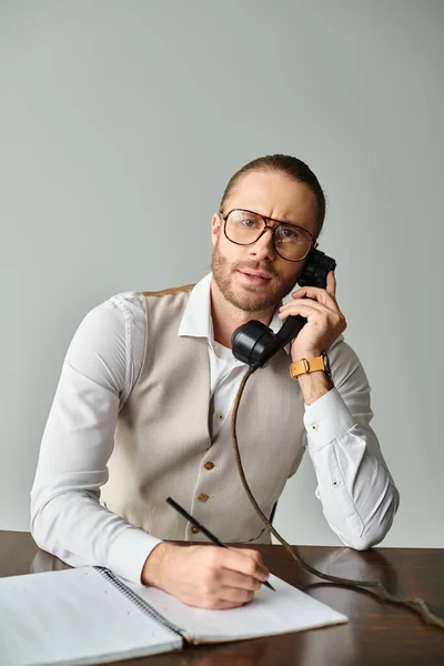Hombre enfocado bien parecido con barba y gafas hablando por teléfono retro y mirando a la cámara - foto de stock