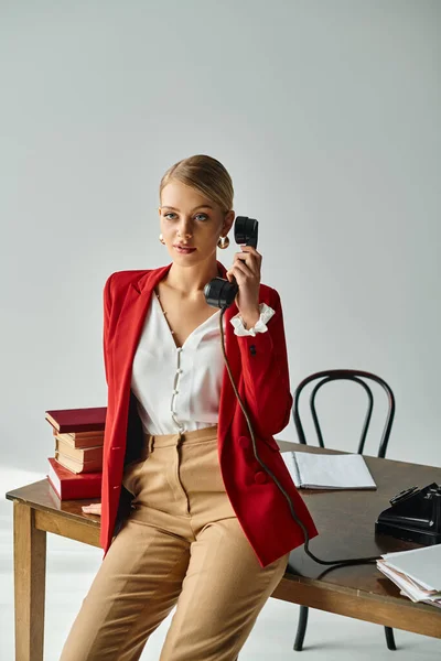 Mujer rubia de buen aspecto en traje vívido hablando por teléfono retro y mirando hacia otro lado en la oficina - foto de stock
