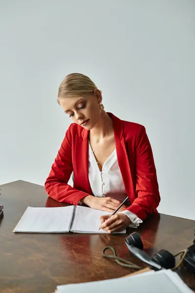 Concentrated young woman in red vibrant jacket taking notes while sitting at table in her office — Stock Photo