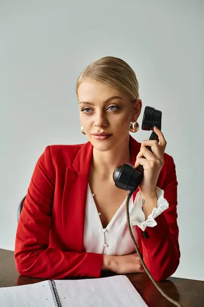Mujer rubia de buen aspecto en chaqueta elegante rojo hablando por teléfono vintage mientras trabaja en la oficina - foto de stock