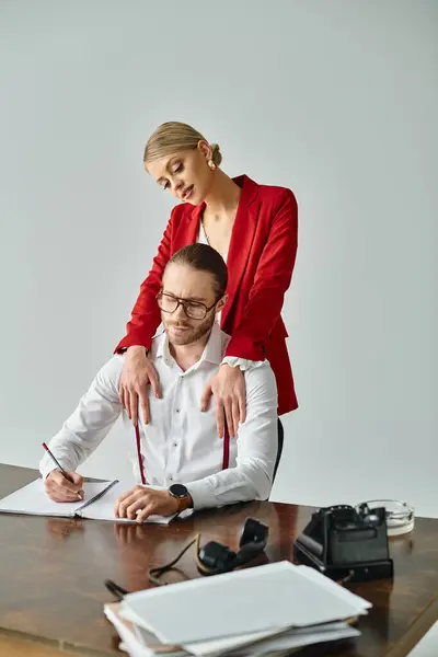 Séduisante femme joyeuse en veste rouge étreignant son patron qui travaille dur au bureau, affaire de travail — Photo de stock