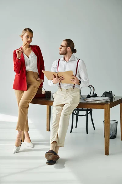 Mujer rubia caliente en chaqueta roja mirando cautivadoramente a su jefe sexy con barba, asunto de trabajo - foto de stock