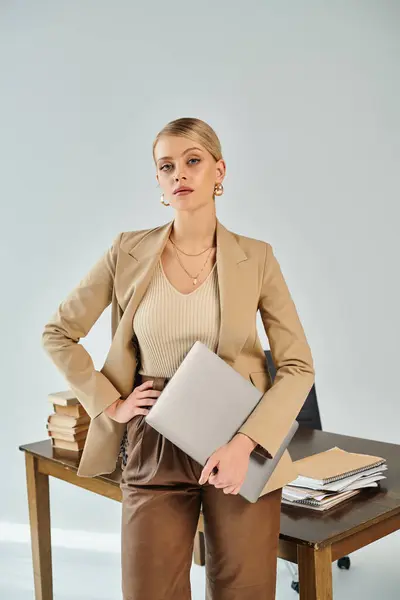 Mulher bonita com acessórios e cabelo loiro em terno elegante segurando laptop e olhando para a câmera — Fotografia de Stock